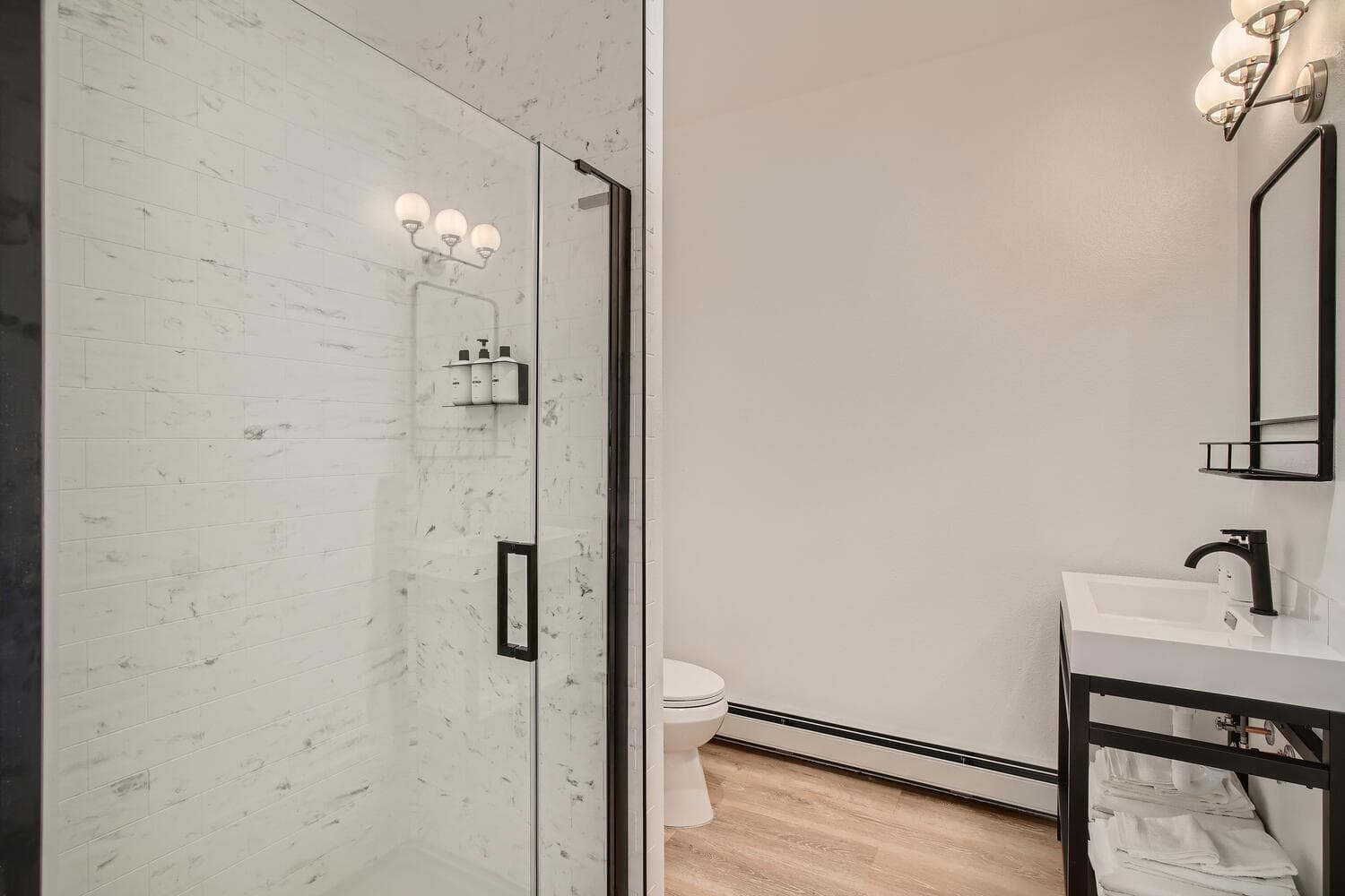 A modern bathroom featuring a glass shower, white vanity, and a toilet.