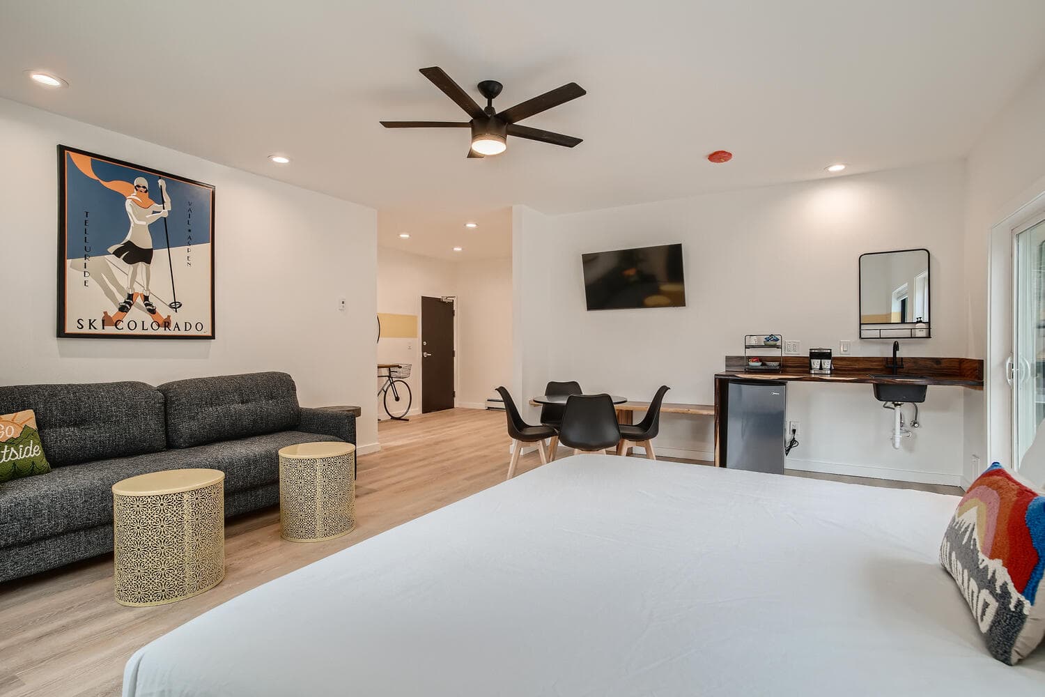 A modern hotel room featuring a bed, sofa, dining area, and wall art.