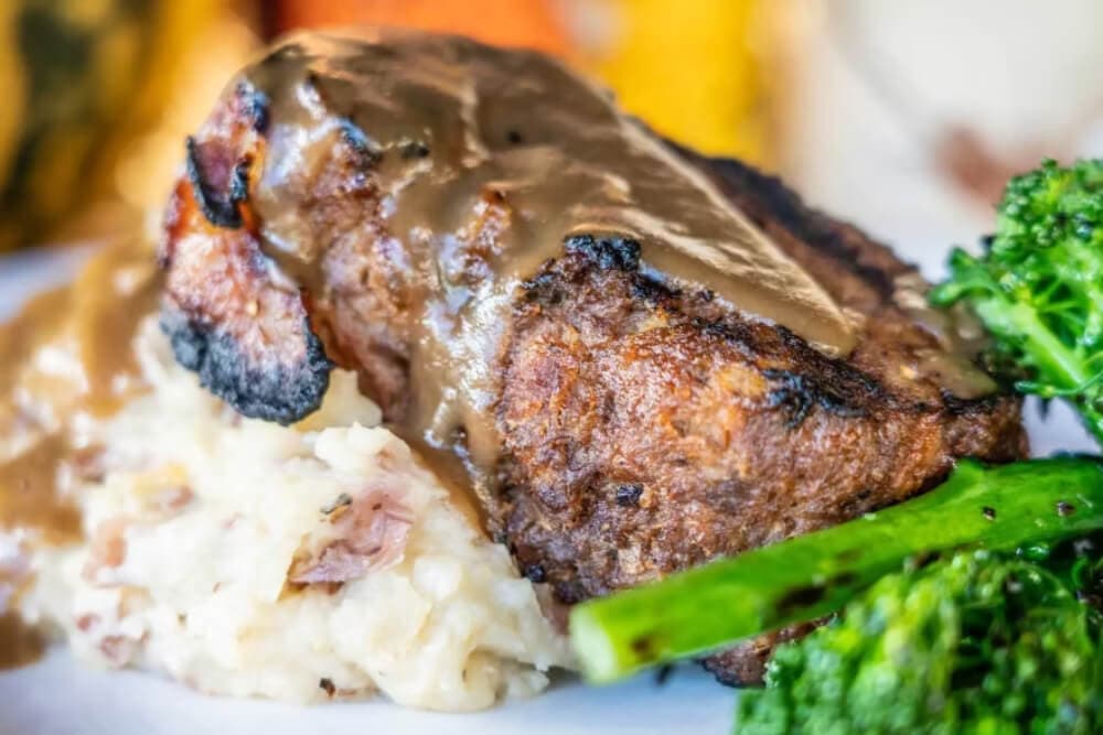 A plate featuring a piece of meatloaf topped with gravy, served alongside mashed potatoes and broccoli.