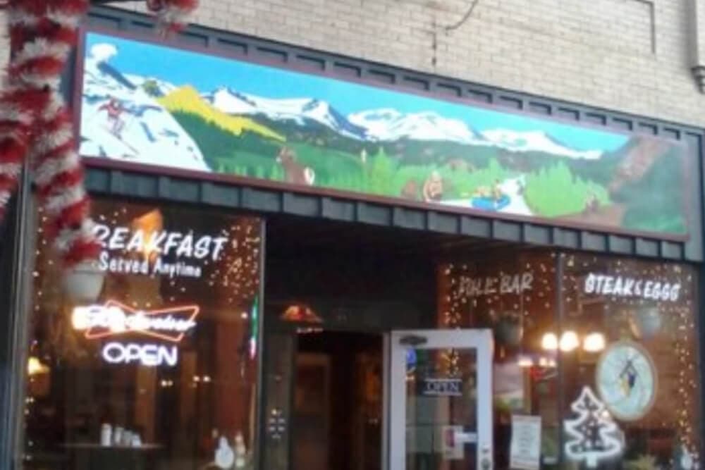 A restaurant exterior featuring a colorful mural of mountains and trees, with illuminated signs for breakfast and steak.