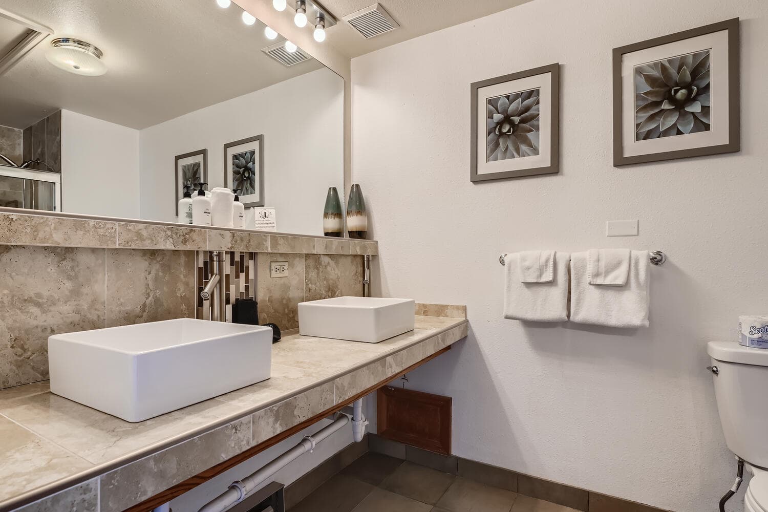 A modern bathroom featuring a double sink, wall art, and neatly arranged towels.