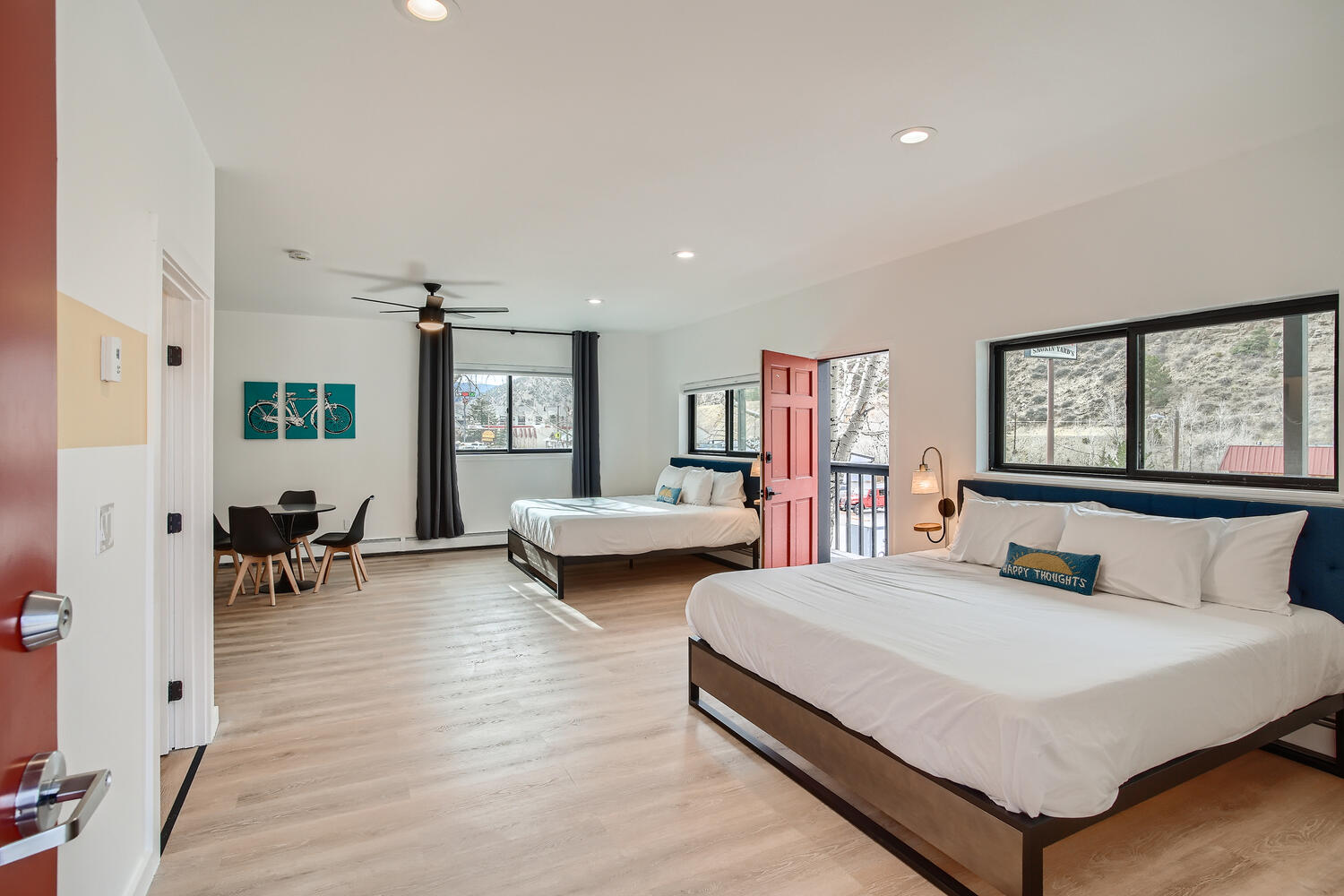 A bright and modern room featuring two beds, a small dining area, and large windows with natural light.