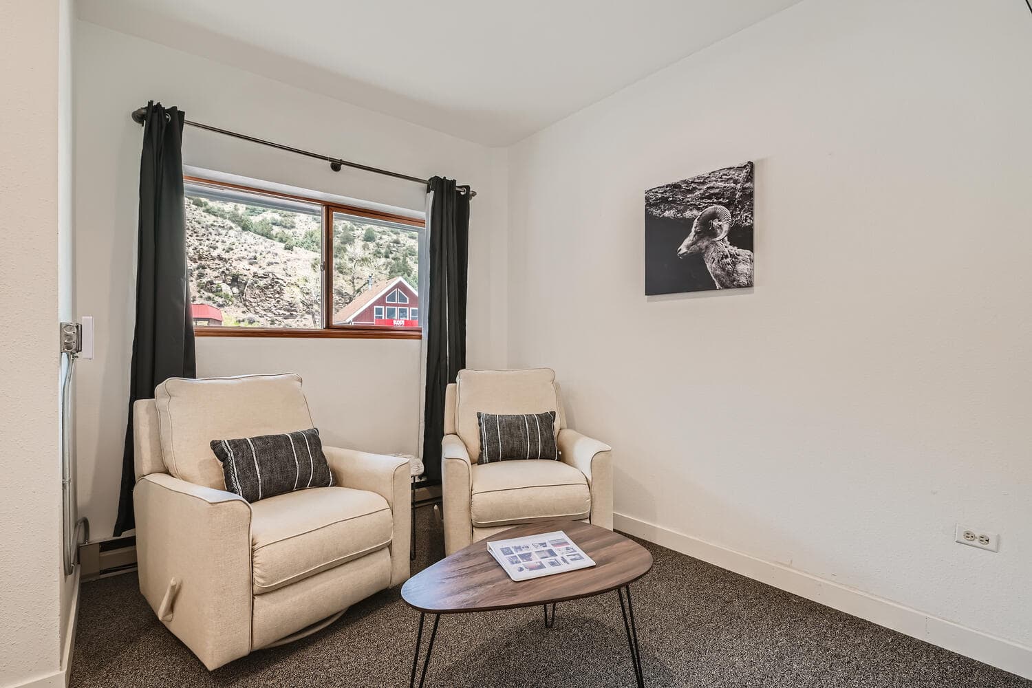A cozy seating area with two armchairs, a coffee table, and a mountain view through the window.