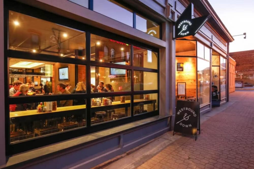 A restaurant with large windows showcasing diners inside, illuminated by warm lighting.