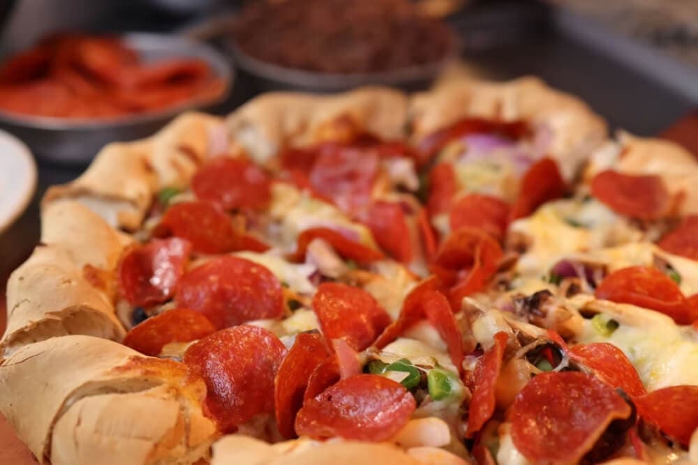 A close-up of a pepperoni pizza with a stuffed crust, surrounded by toppings.