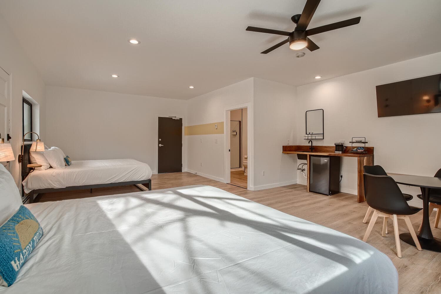 A modern bedroom featuring two beds, a desk area, and a TV.
