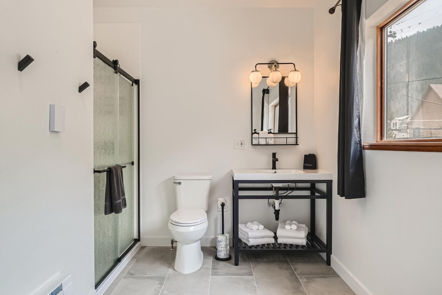 A modern bathroom featuring a shower, toilet, sink with storage, and a window.