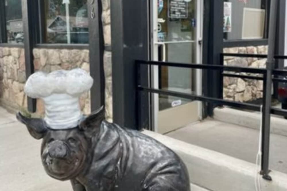 A bronze pig sculpture wearing a chef's hat stands outside a restaurant entrance.
