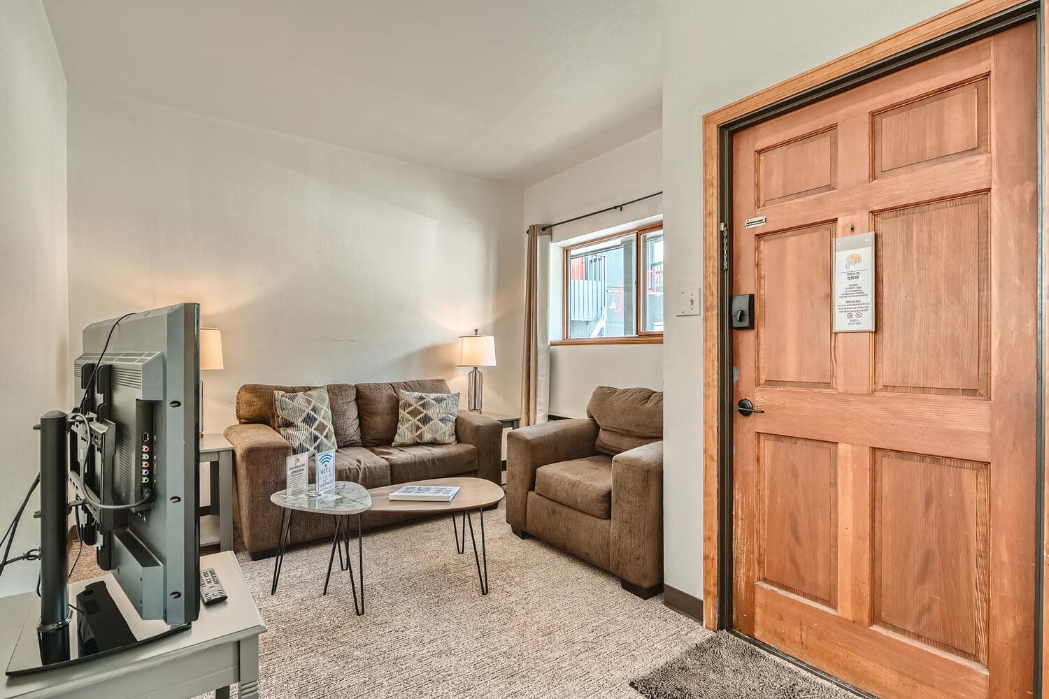 A cozy living space featuring a sofa, armchair, coffee table, and a television near the entrance.