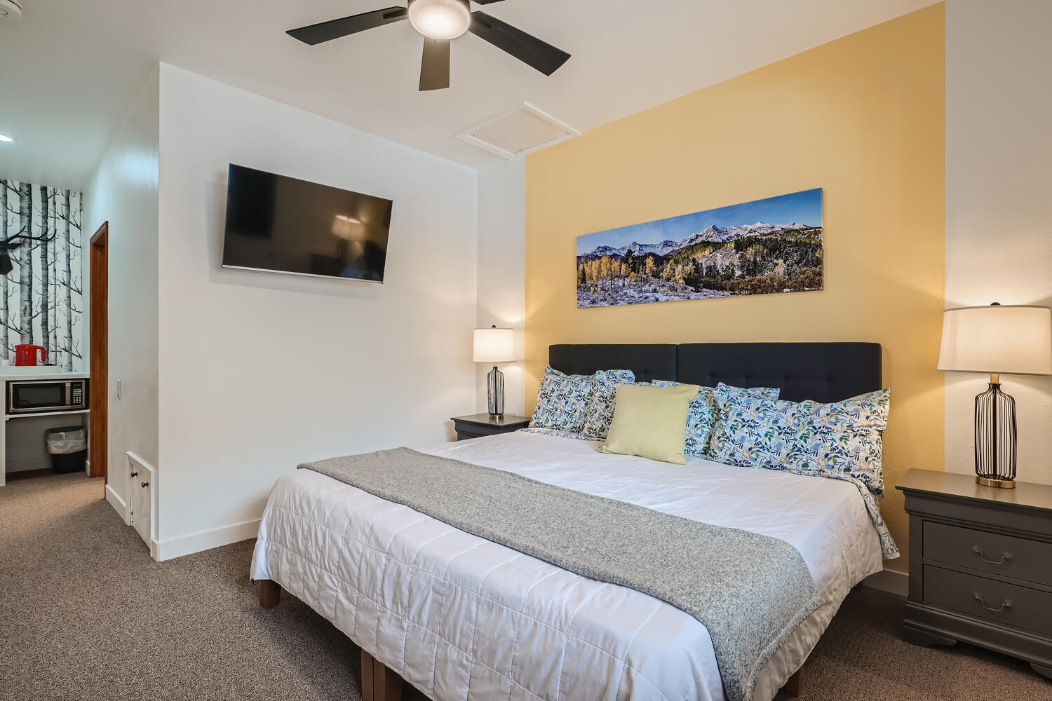 Cozy bedroom featuring a king-sized bed, two lamps, a television, and mountain artwork on the wall.