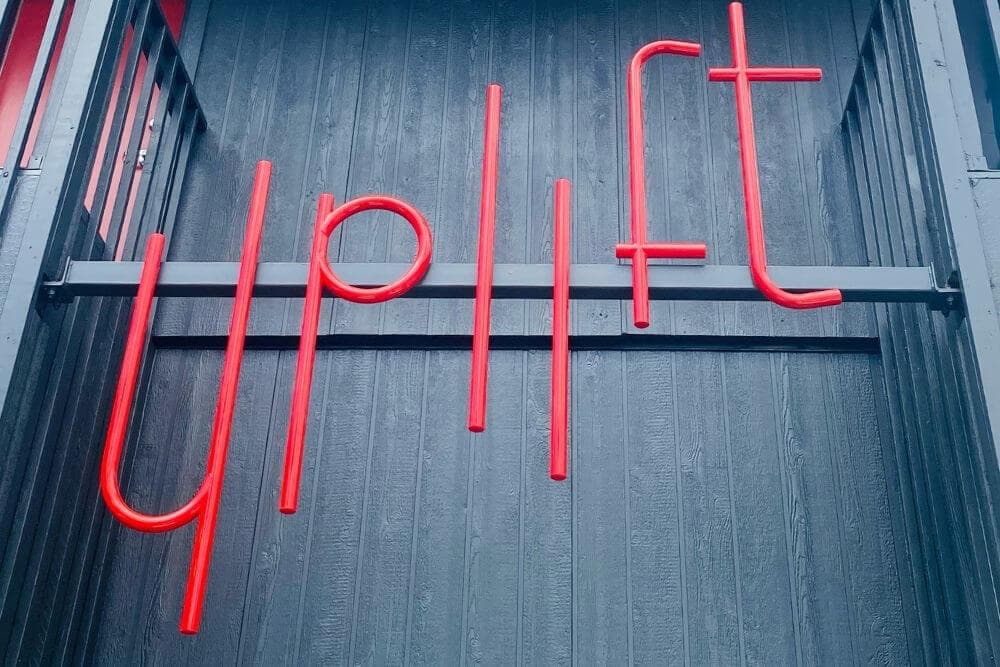 Red neon sign reading "uplift" against a dark wooden background.