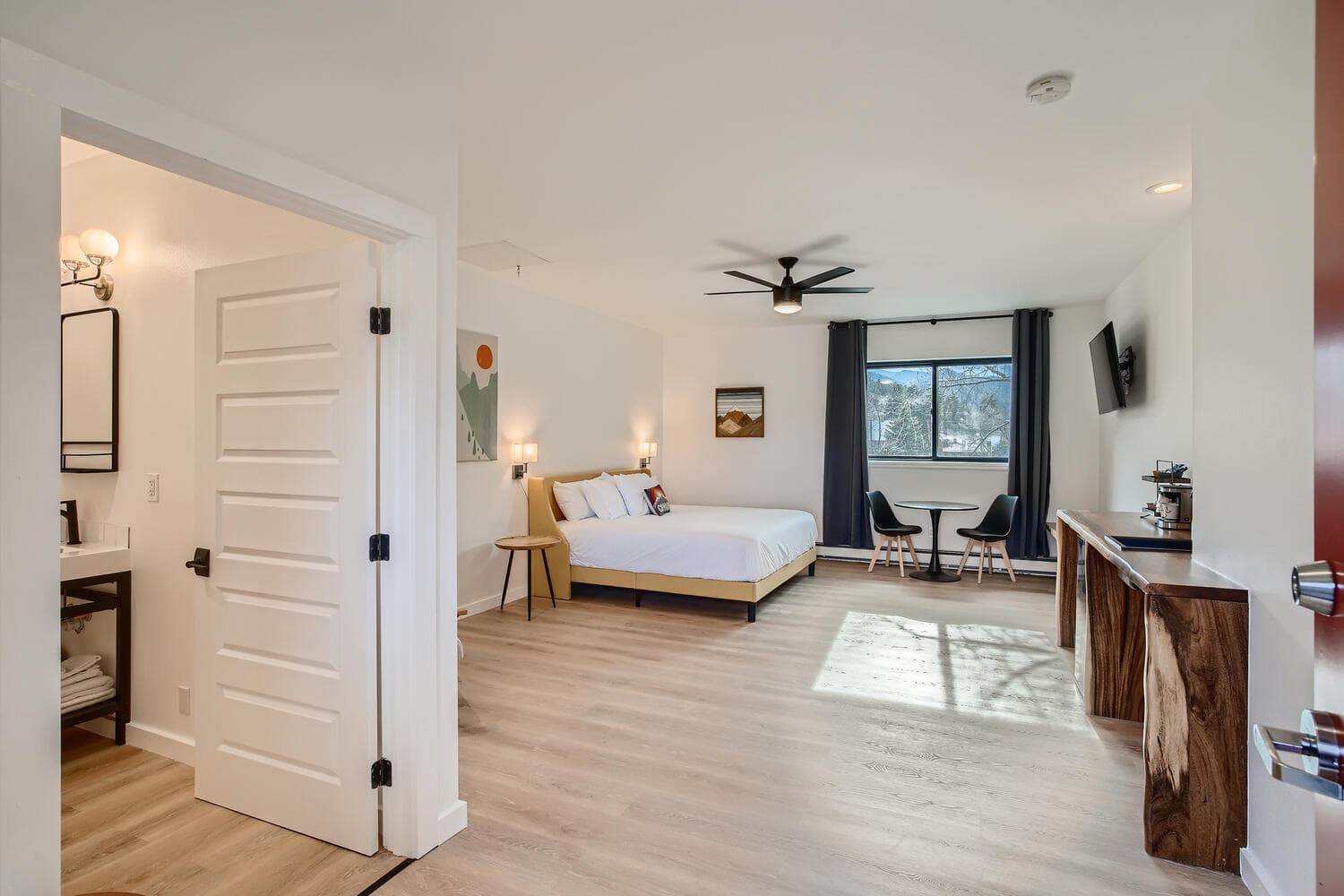 A modern hotel room featuring a king-sized bed, a seating area by a window, and minimalistic decor.