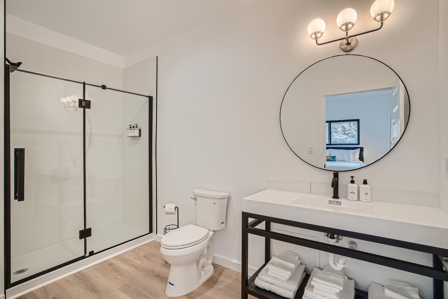 Modern bathroom featuring a glass shower, a sleek vanity with toiletries, and a round mirror.