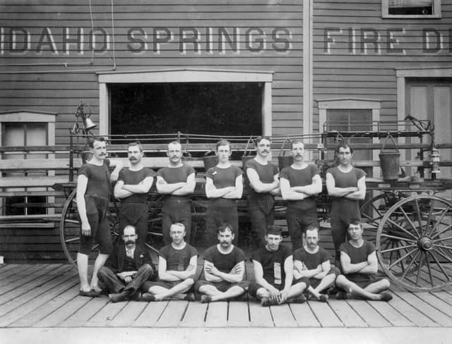 Historic 1895 Idaho Springs Fire Department firefighters posing outside station with antique fire wagon and equipment in Idaho Springs, Colorado
